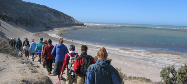 Photo of a group of hikers walking single-file on a beach