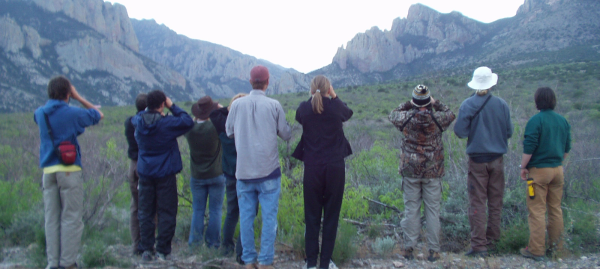 Photo of a group of people standing in a mountainous area with binoculars