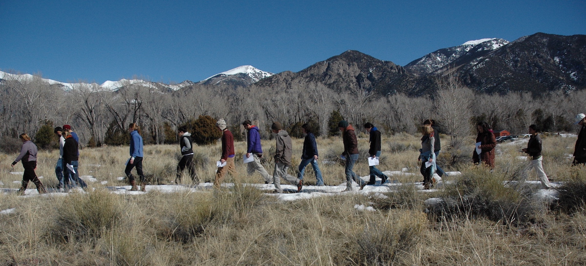 A college class of students hiking through some brush in Crestone, Colorado