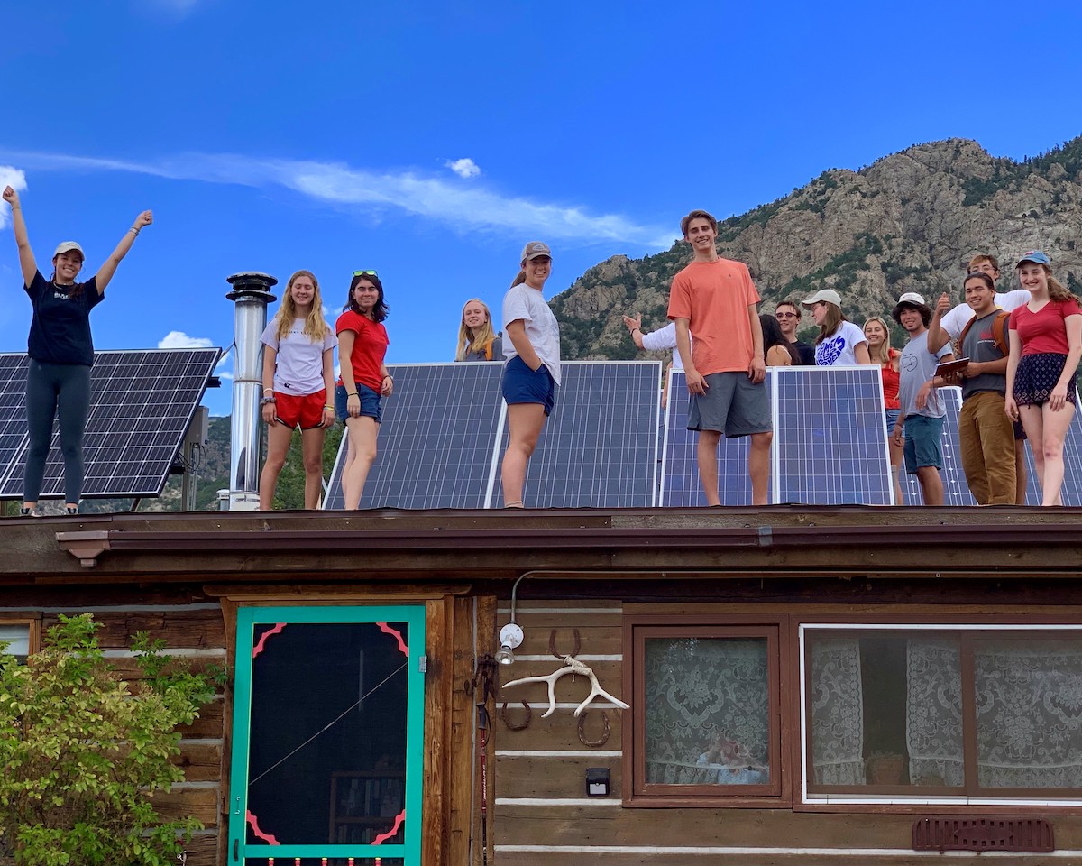 college students on top of a roof next to newly installed solar panels and celebrating