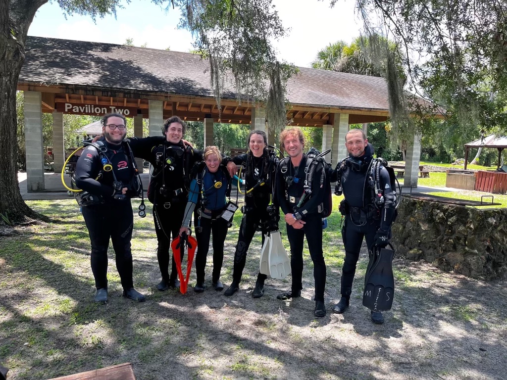 Group photo with 6 people in their scuba gear on land. 