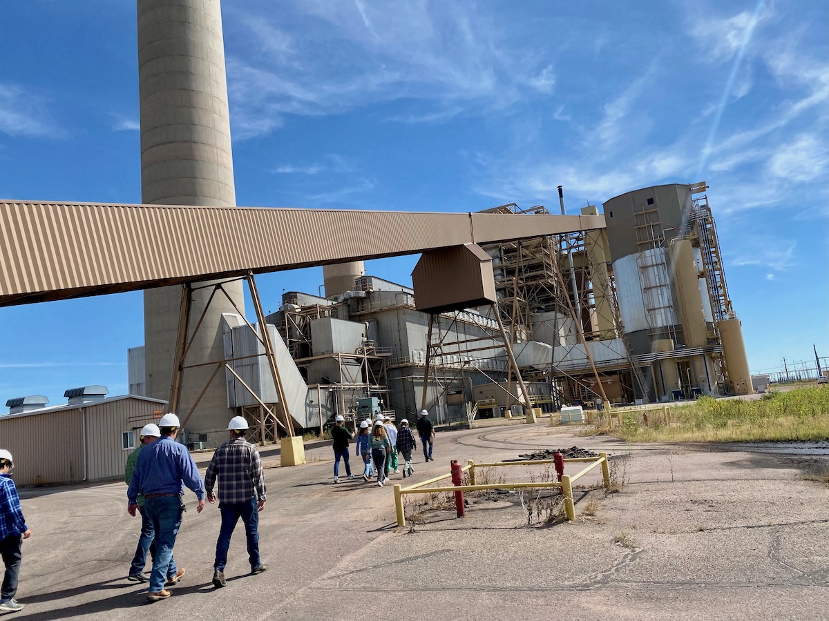 People walking around an industrial structure wearing hard hats