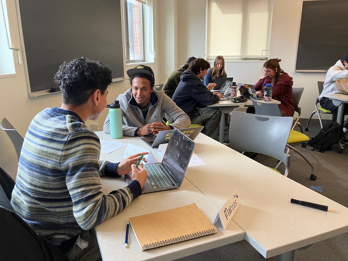 Students sitting in groups at tables discussing classwork