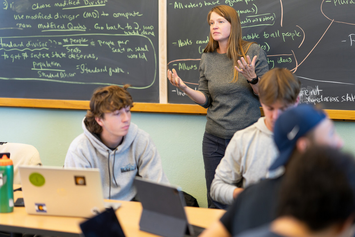 Beth Malmskog teaching to a class in front of a blackboard