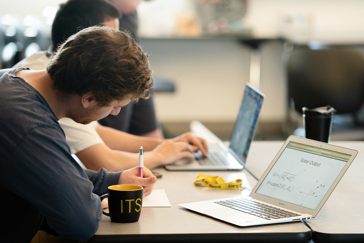 A college student working at a desk with a laptop on a Sobel Output equation 