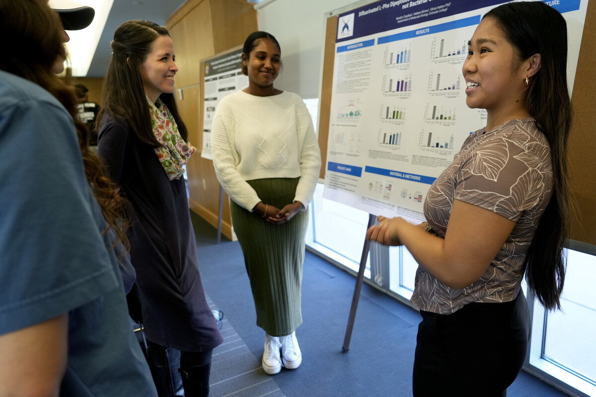 Student presenting their research on a poster board for onlookers