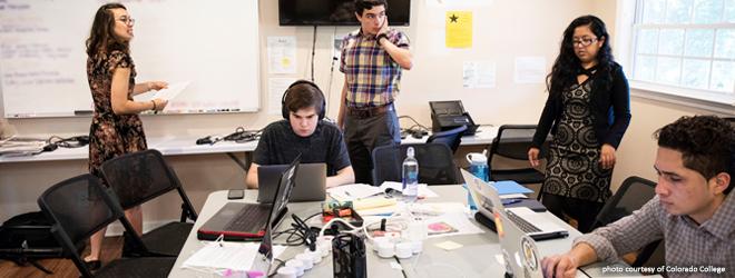 Student working inside an office-like space, seating and standing with documents. 