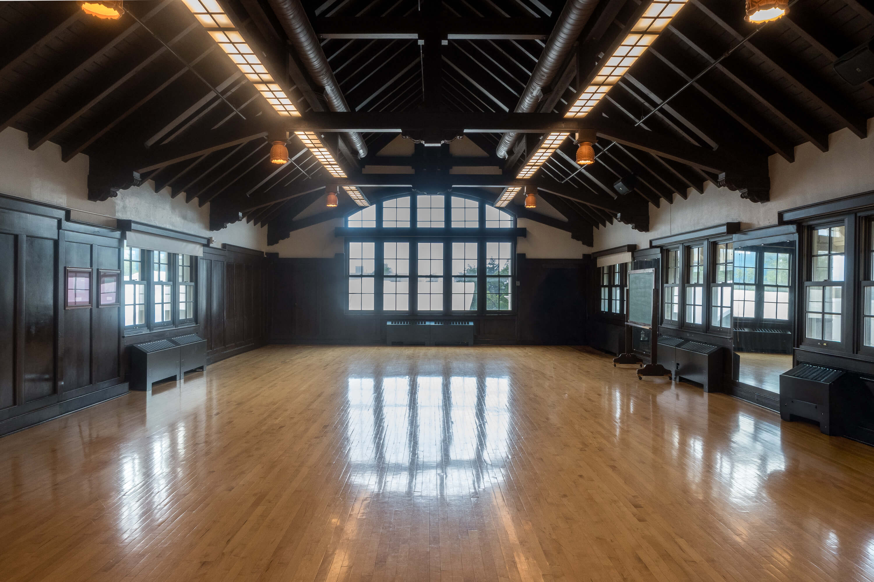 Interior of Cossitt South Studio, featuring a polished wood floor, dark wood paneling, high vaulted ceiling, mirrors, and large windows providing natural light.