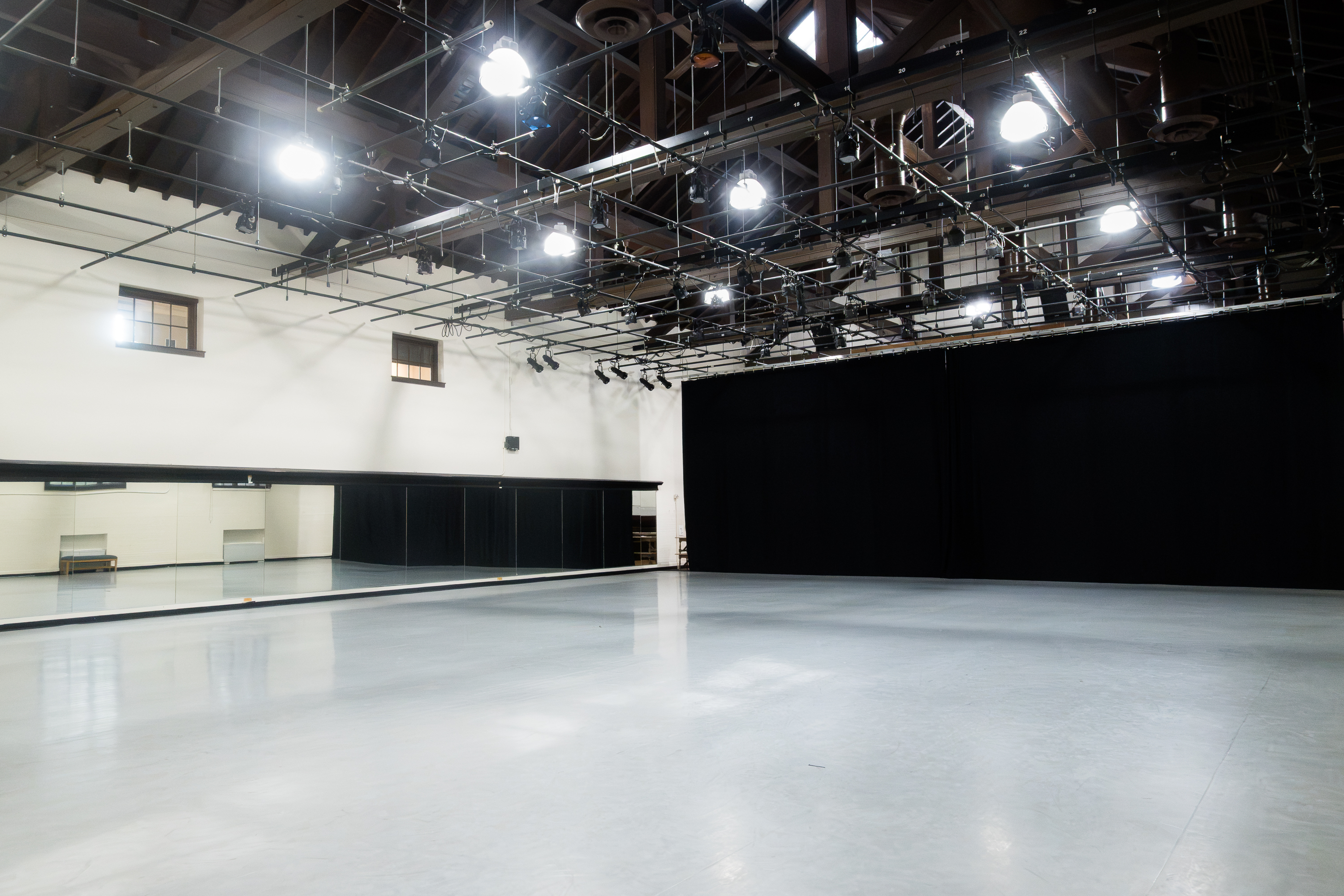 Interior of the Cossitt Gym, featuring a large open dance floor, mirrored wall, black curtains, and extensive overhead theatrical lighting.