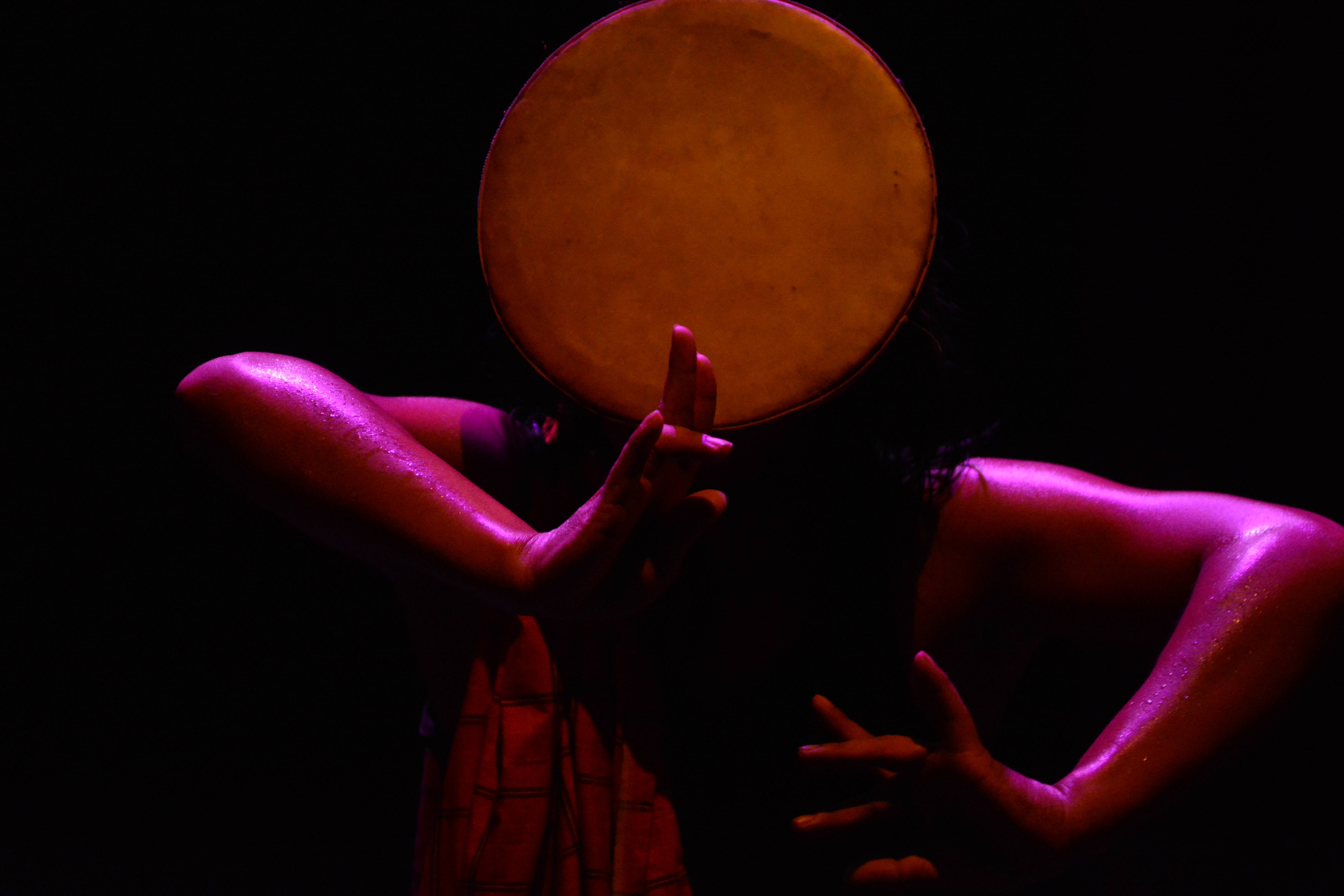 Rianto performing under pink and red stage lighting, framed by a large circular prop and another dancer’s extended arms.
