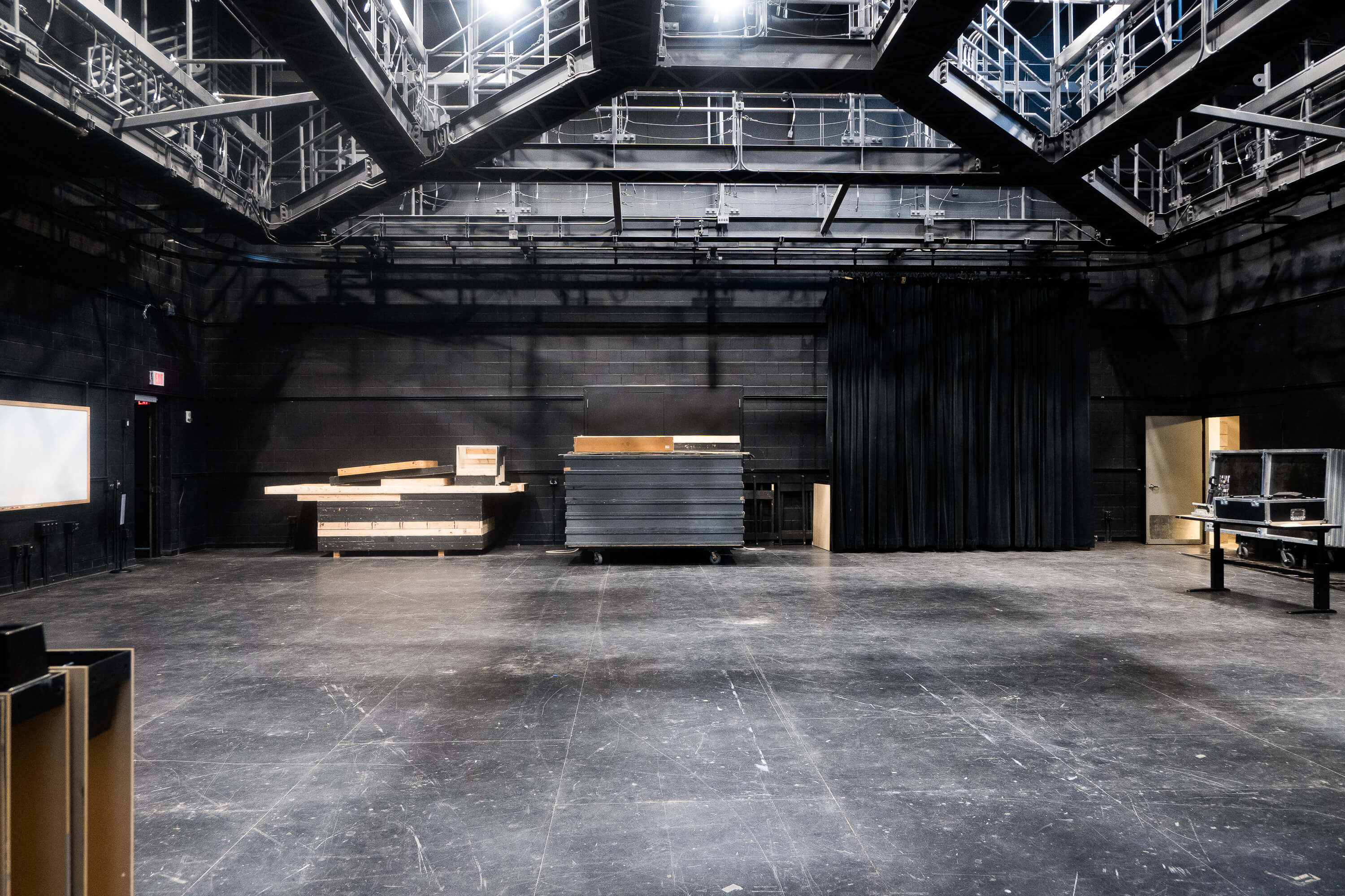 Interior of Norberg Studio A, a black box performance space with a large open floor, black walls, overhead lighting and rigging, curtains, and movable staging platforms.