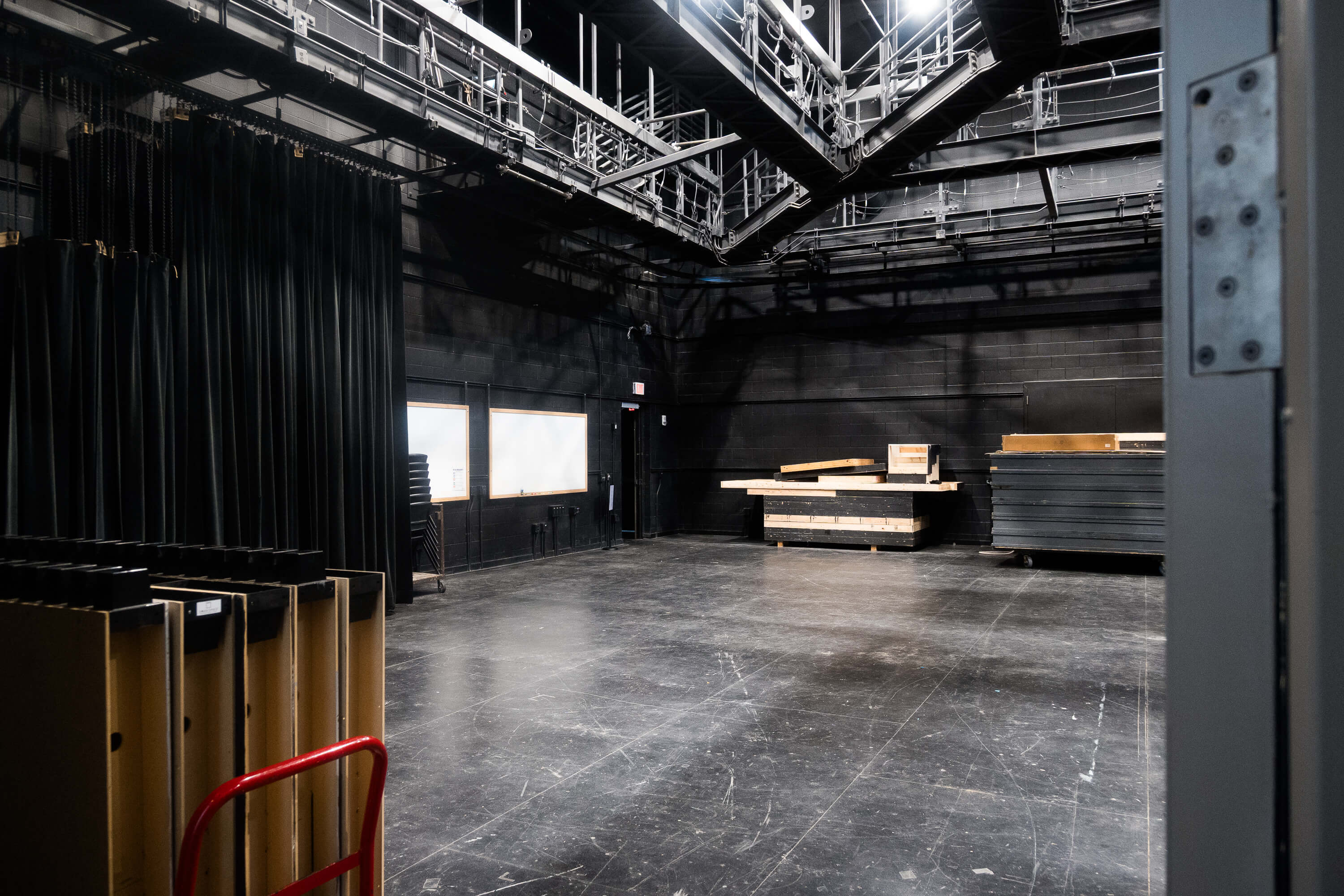 Interior of Norberg Studio A, a black box performance space with a large open floor, black walls, overhead lighting and rigging, curtains, and movable staging platforms.