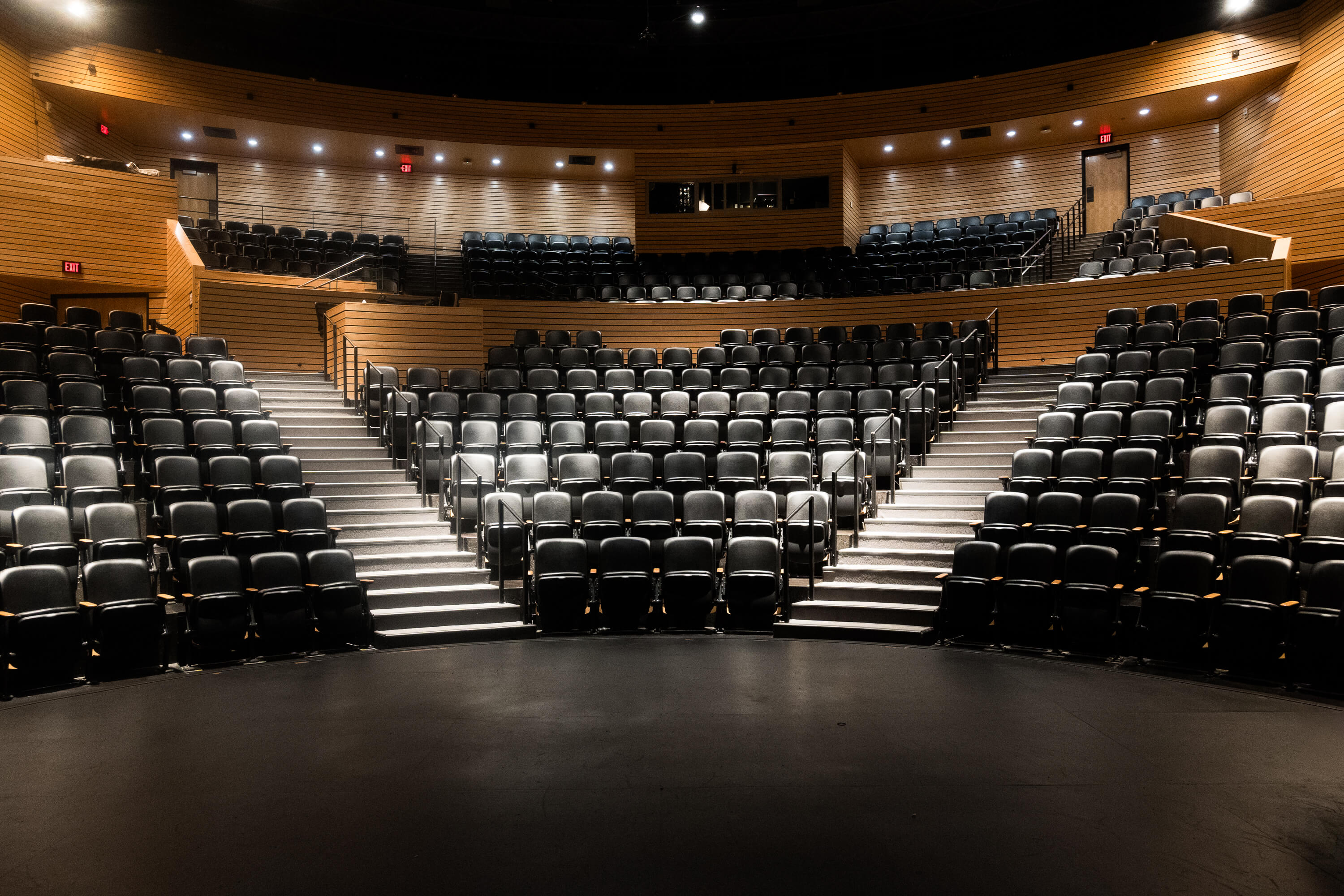 Interior view of the Cornerstone Arts Center’s Richard F. Celeste Theatre, showing tiered black seating, wood-paneled walls, aisles, and the stage floor.