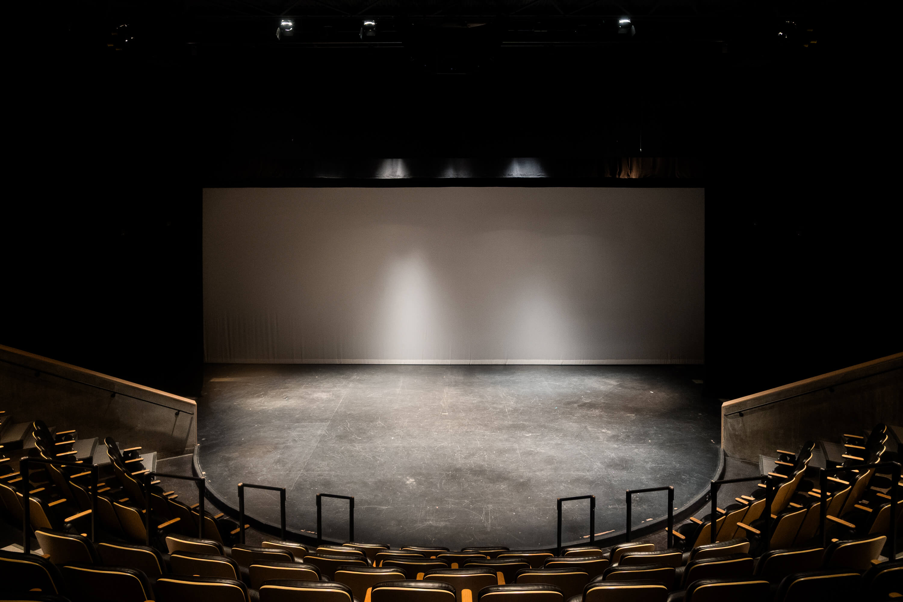 Interior view of the Cornerstone Arts Center’s Richard F. Celeste Theatre, showing tiered black seating, wood-paneled walls, aisles, and the stage floor.