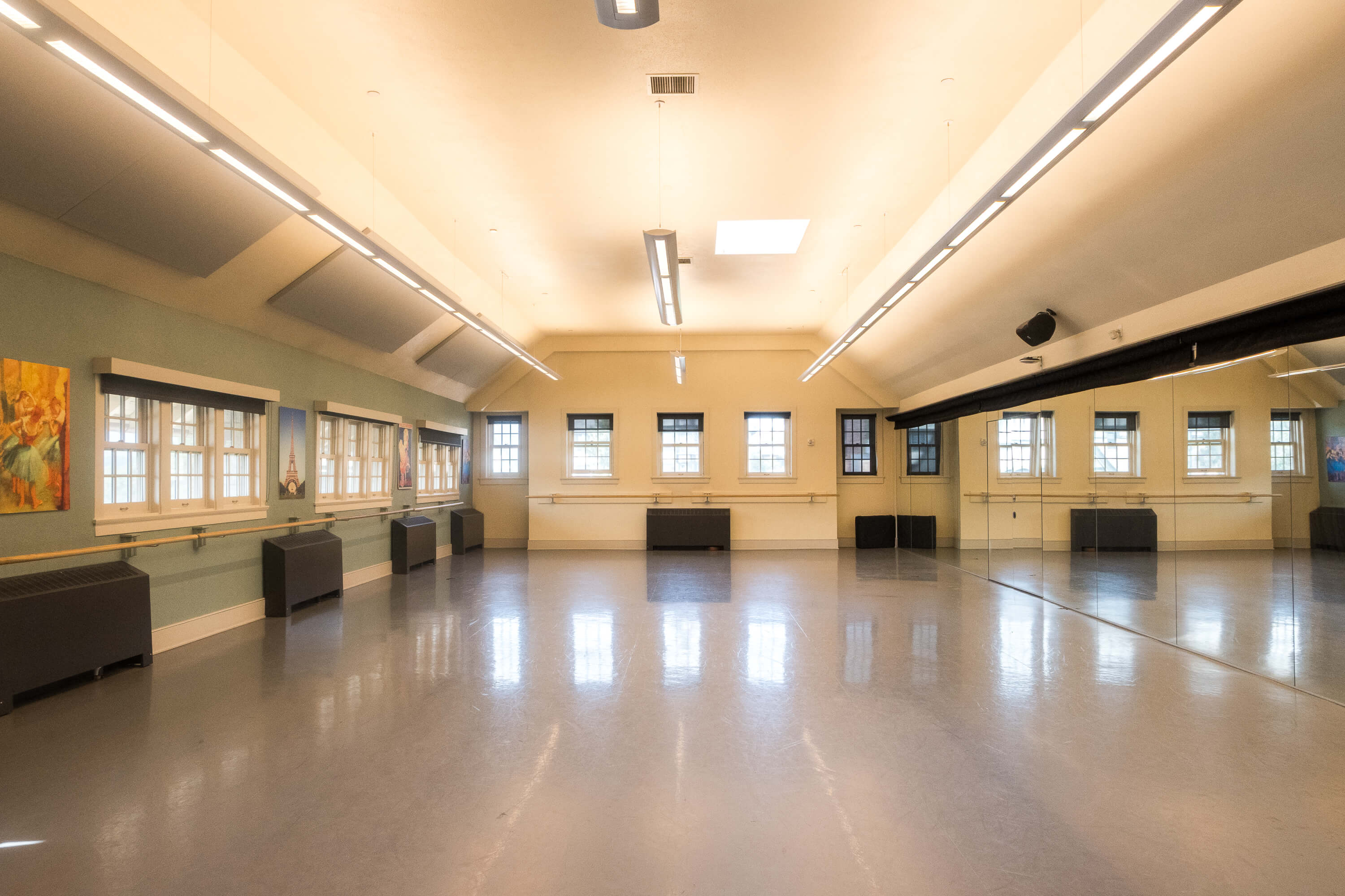 Interior of Cossitt North Studio, featuring a spacious dance floor, mirrored wall, ballet barres, and large windows providing natural light.
