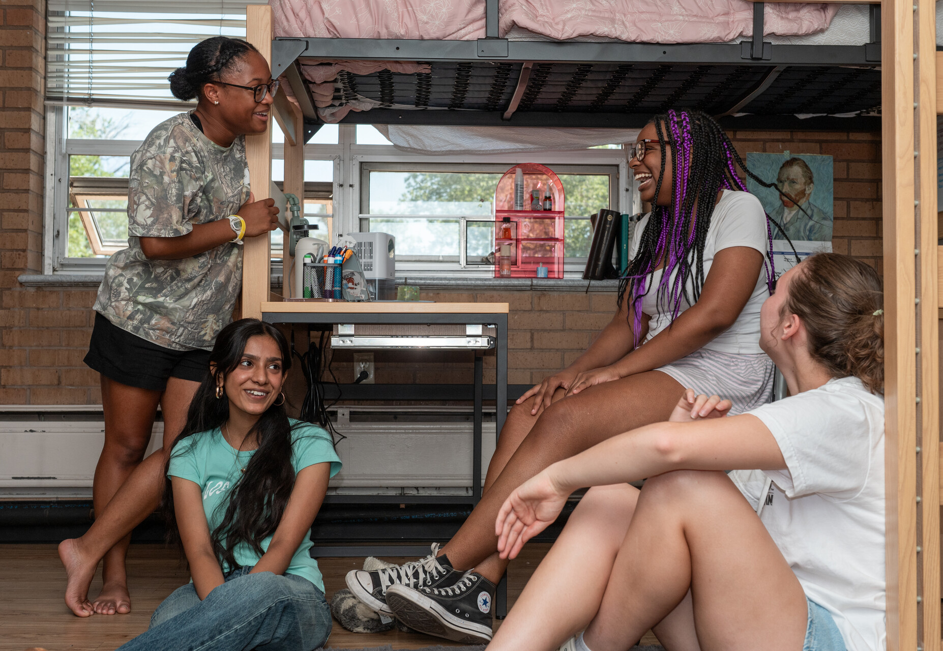 Group of students socializing in CC housing, next to a bed and dresser.