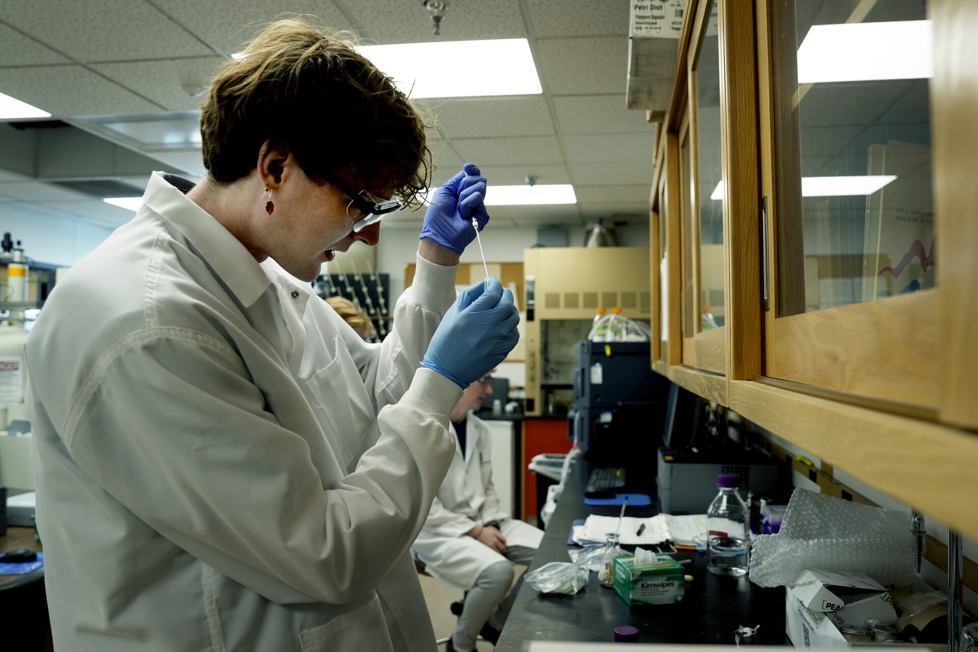 Student in lab coat and goggles performing research in a chemistry lab