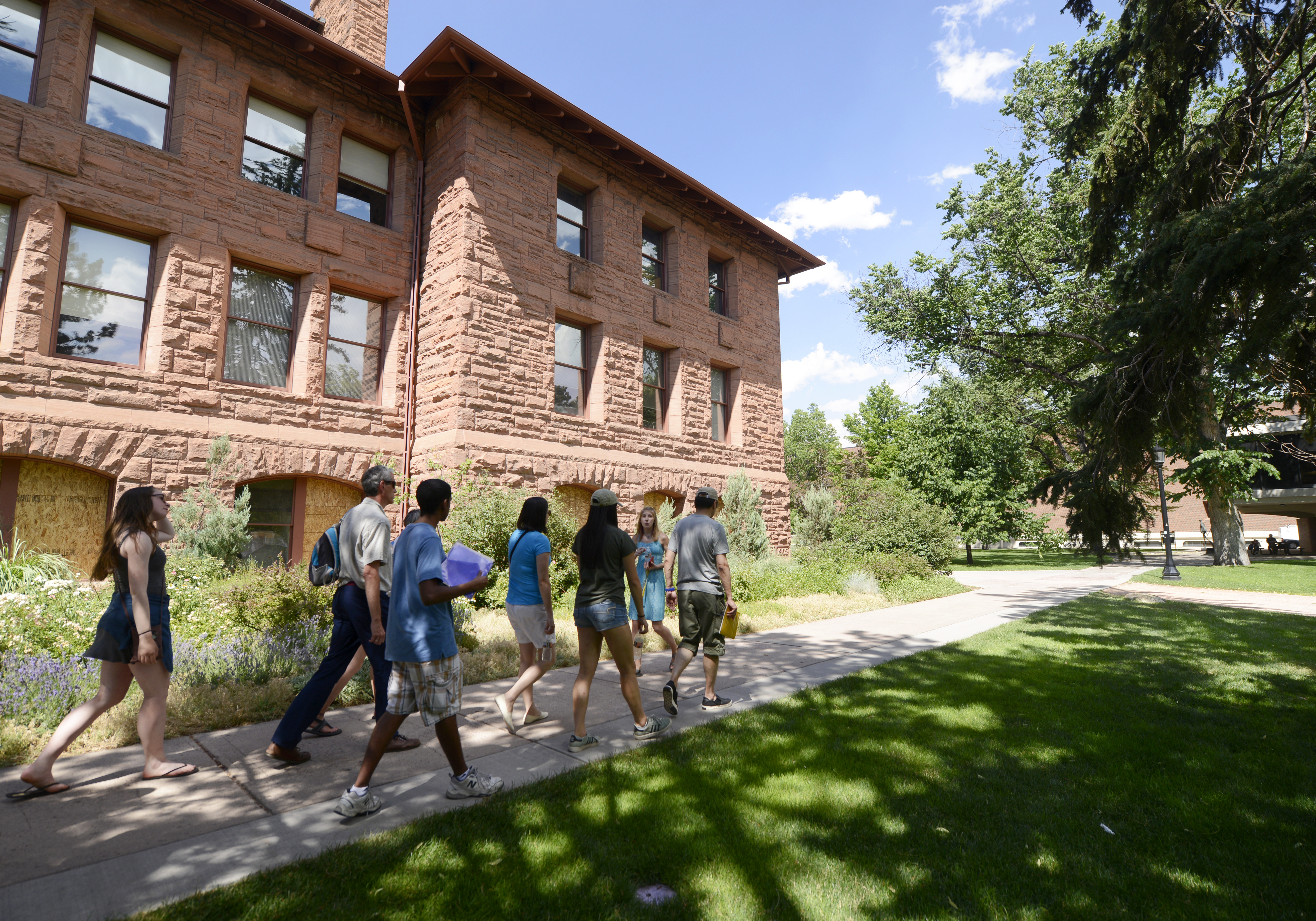 Group of prospective students on a tour, led by a current student. Background features a historic stone building with green grass and trees.