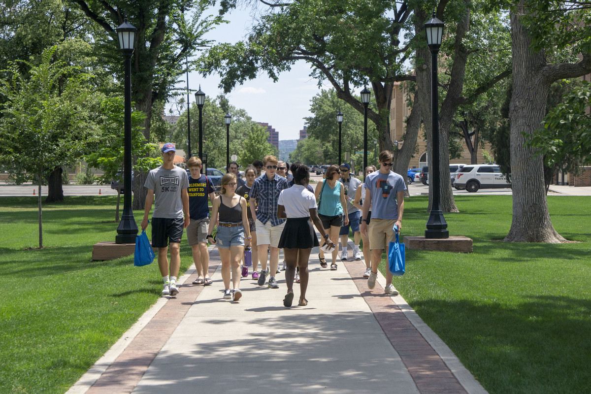 CC student walks backward while leading a tour group of prospective students and parents through Tava Quad