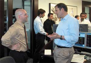 Assistant Professor John Stinespring (foreground, left) discusses strategy for buying and selling stocks, currencies, and other financial instruments with Troubh Hedge Fund partner <strong>John Troubh ’79</strong> during a 2004 field trip. Behind them, Money, Banking, and Financial Markets class members <strong>Kaloyan Kapralov ’05</strong>, <strong>Glenn Carlson ’06</strong>, <strong>Astrid Brouillard ’06</strong>, and <strong>Scott Weaver ’06</strong> watch real-time trading and learn about indicators (such as Federal Reserve Bank announcements, company earnings reports, and news on current events) that cause the markets to move.