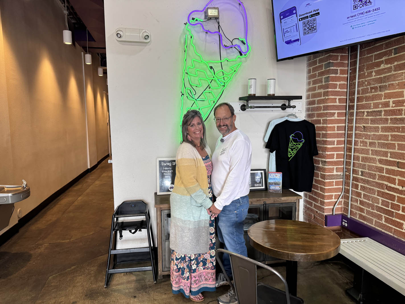 Lindsay Keller and John Krakauer ’85, co-owner of Josh & John’s, stand under the neon ice cream sign in the downtown location as a nod to their wedding photo from 2011. Photo by Khloe Haney/Colorado College.