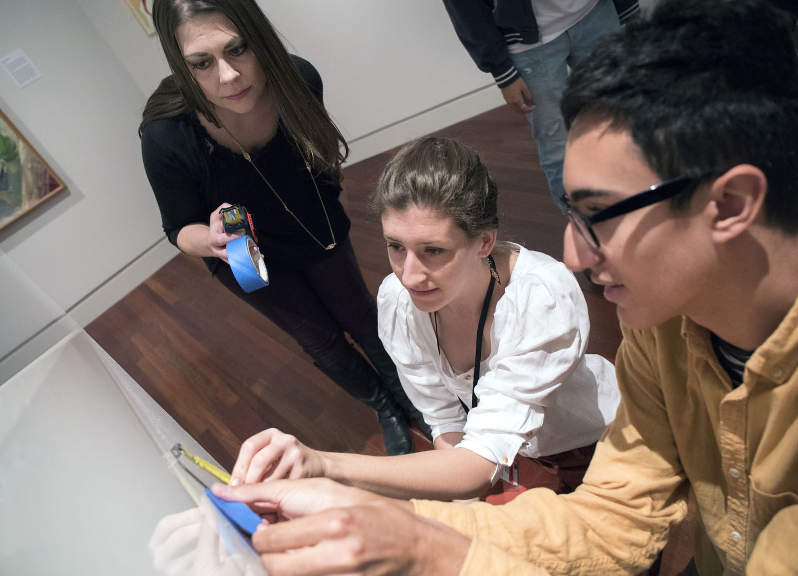Visiting Assistant Professor of Art History Victoria Ehrlich, Fine Arts Center Academic Engagement Assistant Eliza Scally and FYE student <b>Honor Miles '21</b> measure and place the information card that Miles prepared for the FYE curated exhibit.
