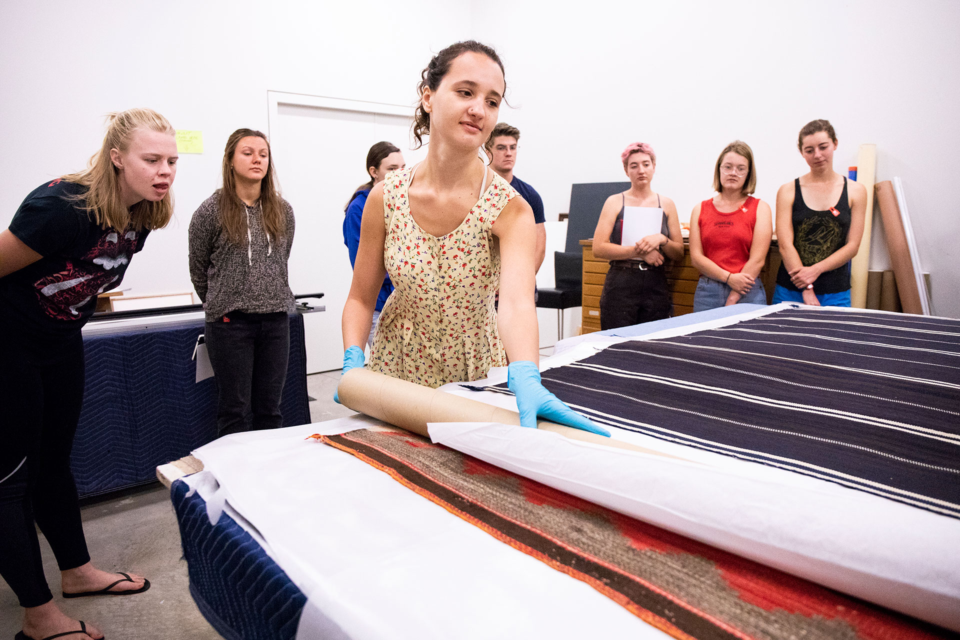 Fine Arts Center intern Amber Mustafic ’19 carefully rolls out a Navajo blanket that is in the collection at the museum so that students in Jeanne Steiner's Fiber Arts class could examine the pieces and look at their structures.