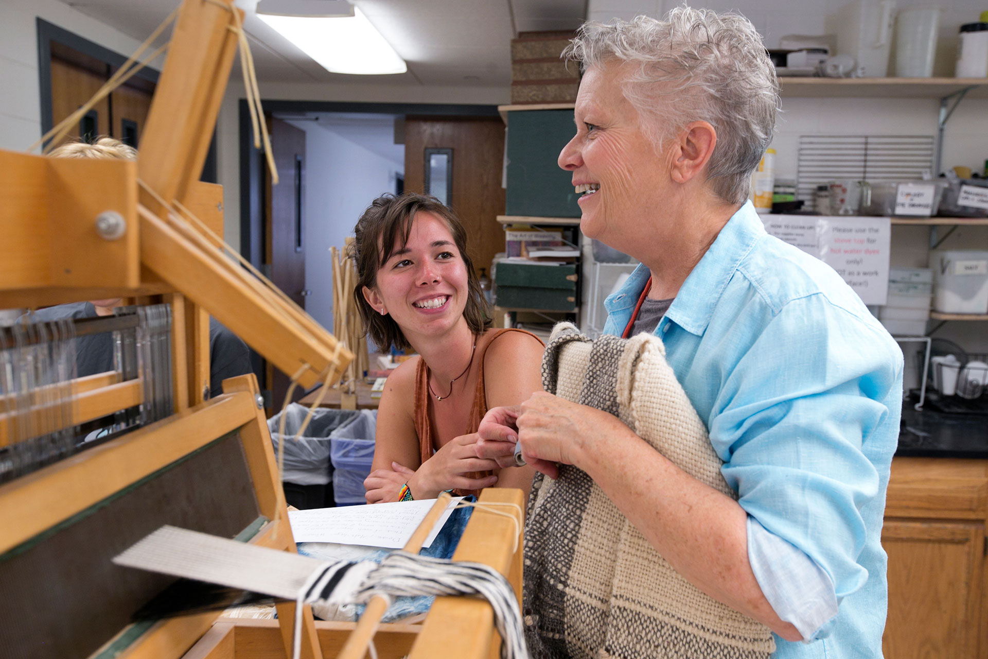 Kai Hill '18 speaks with Fiber Instructor Jeanne Stiener about her double-weaved jacket created when she was a student after a loom demonstration on how to double weave yarns.