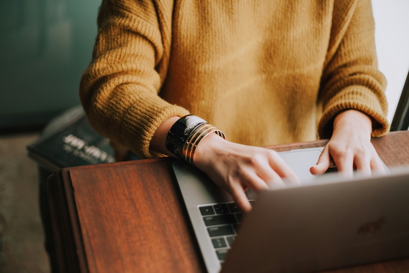 woman in yellow sweater sitting at a desk behind a laptop