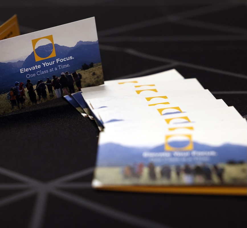 Close up of a folded card that says "Elevate Your Focus. One Class at a Time. with an image of a class in a field in front of a mountain
