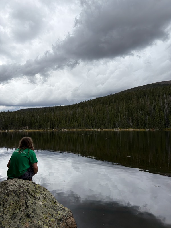 A participant from the Wild Basin Foot Trip sitting in front of a lake. 