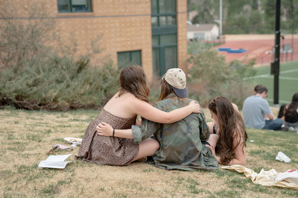 A pair of students with their arms around each other, sitting in the grass  <span class="cc-gallery-credit">[Gray Filter Photography]</span>