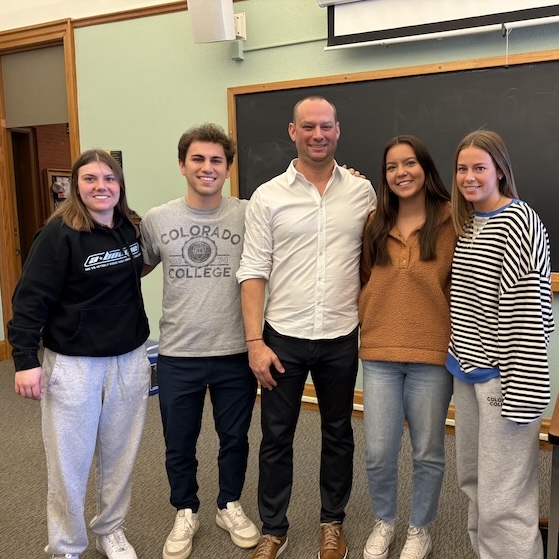 A group of students and a guest client pose at the front of the classroom