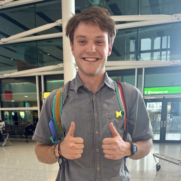 Dan Schmidt stands wearing a backpack and giving 2 thumbs up